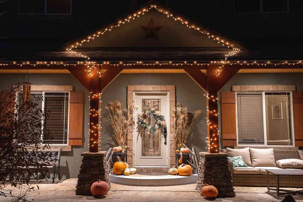 Christmas lights with pumpkins and and wreath on the front door of a home