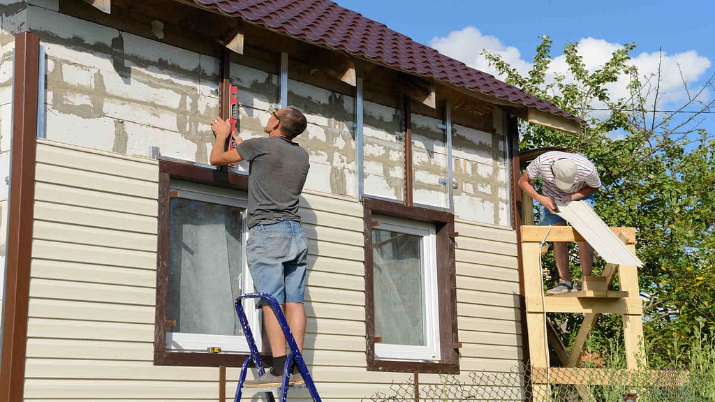 Two people installing a vinyl siding 