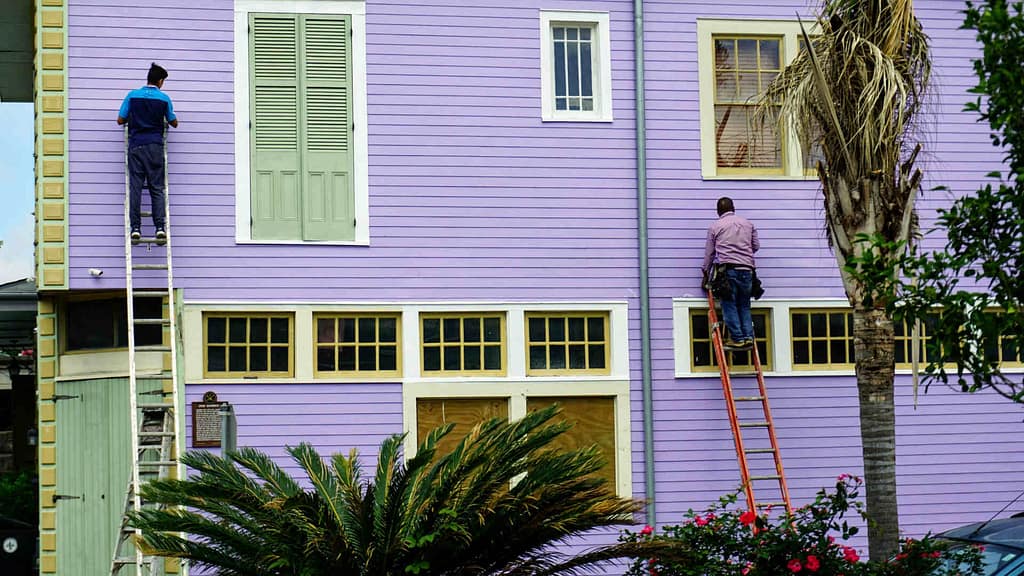 two people painting a siding of a house with purple color