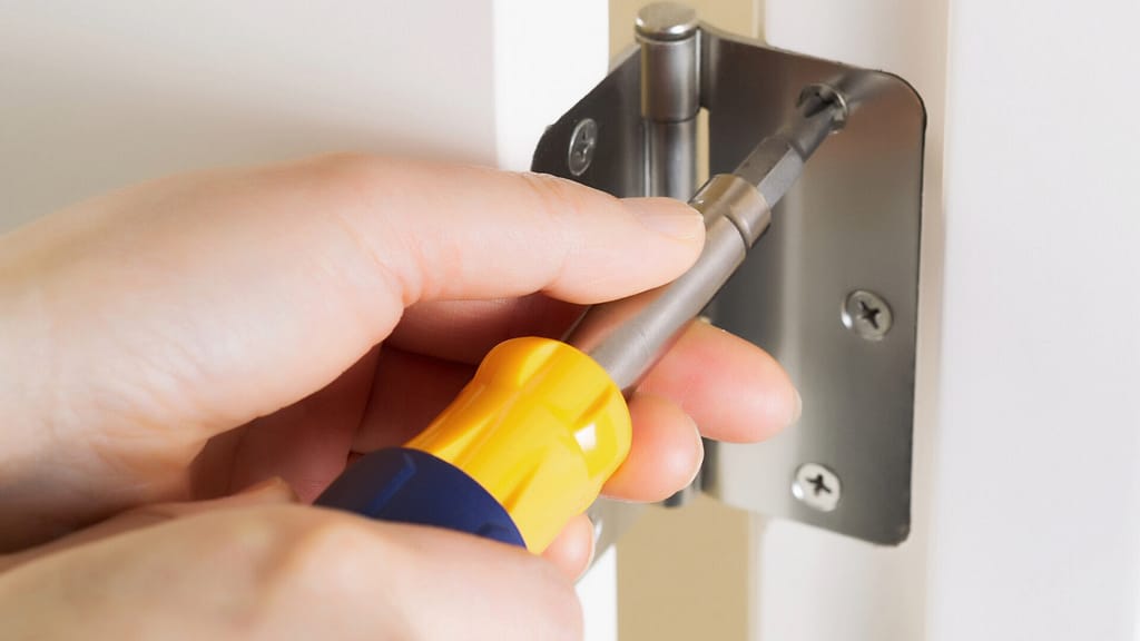 person tightening the screw on a door hinge using a screwdriver