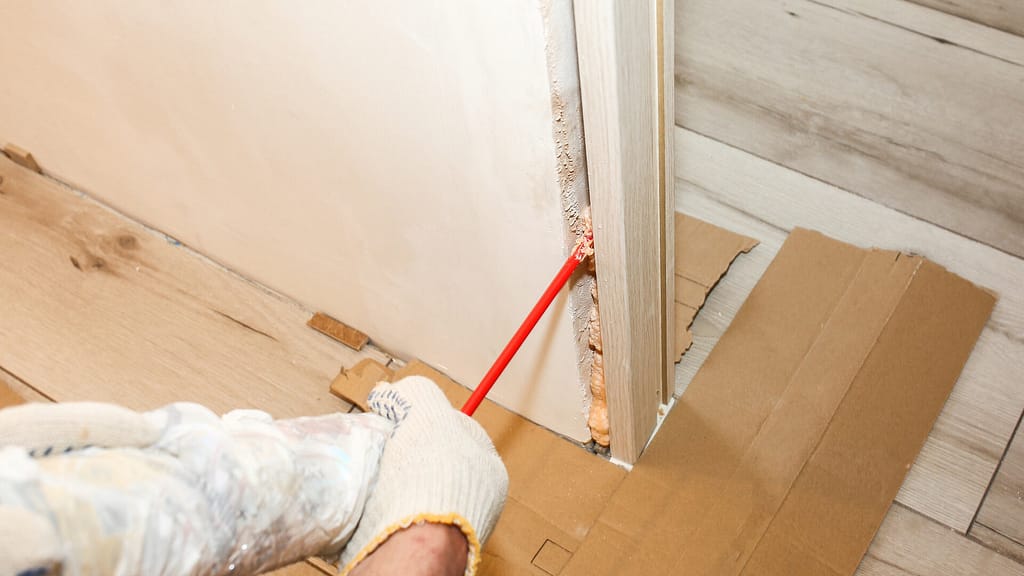 Person putting foam insulation to the gaps between the door frame and wall