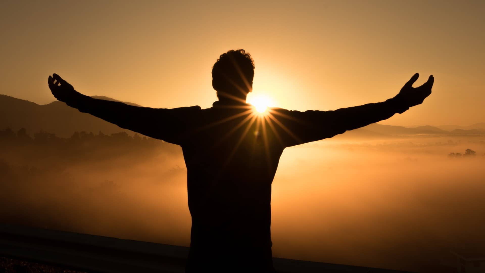 man with arms out facing sun