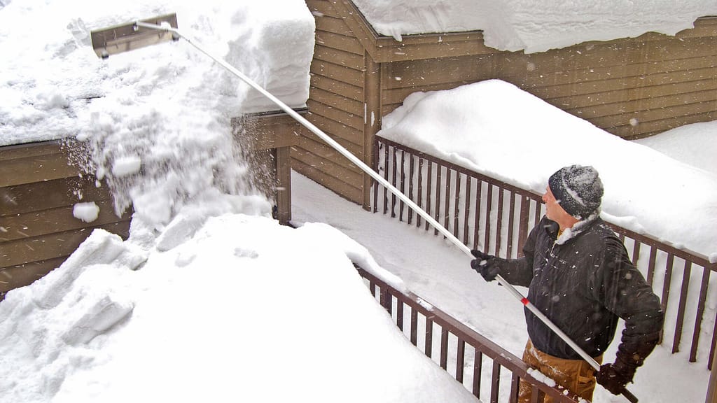 man using a rake to remove snow off the roof